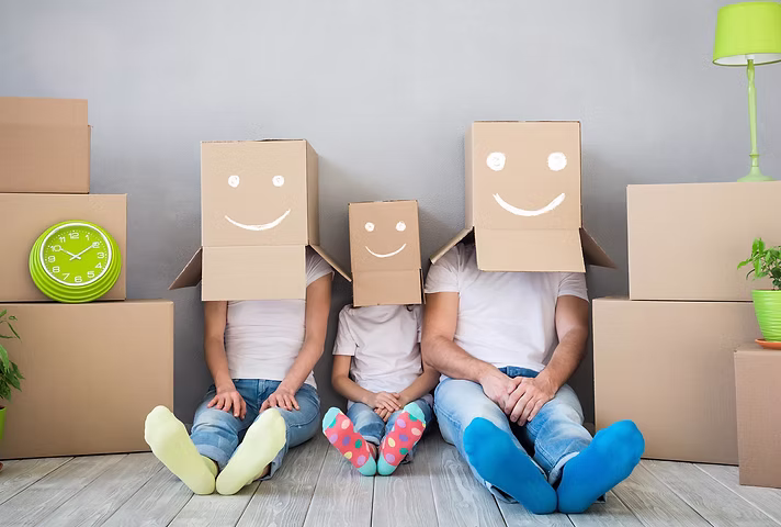 family sitting on floor with cardboard boxes over their heads during home move